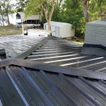 Black metal roof, freshly installed. Daylight illuminates trees in the background.
