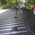 Black metal roof, freshly installed. Daylight illuminates trees in the background.