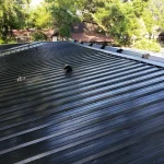 Black metal roof, freshly installed. Daylight illuminates trees in the background.